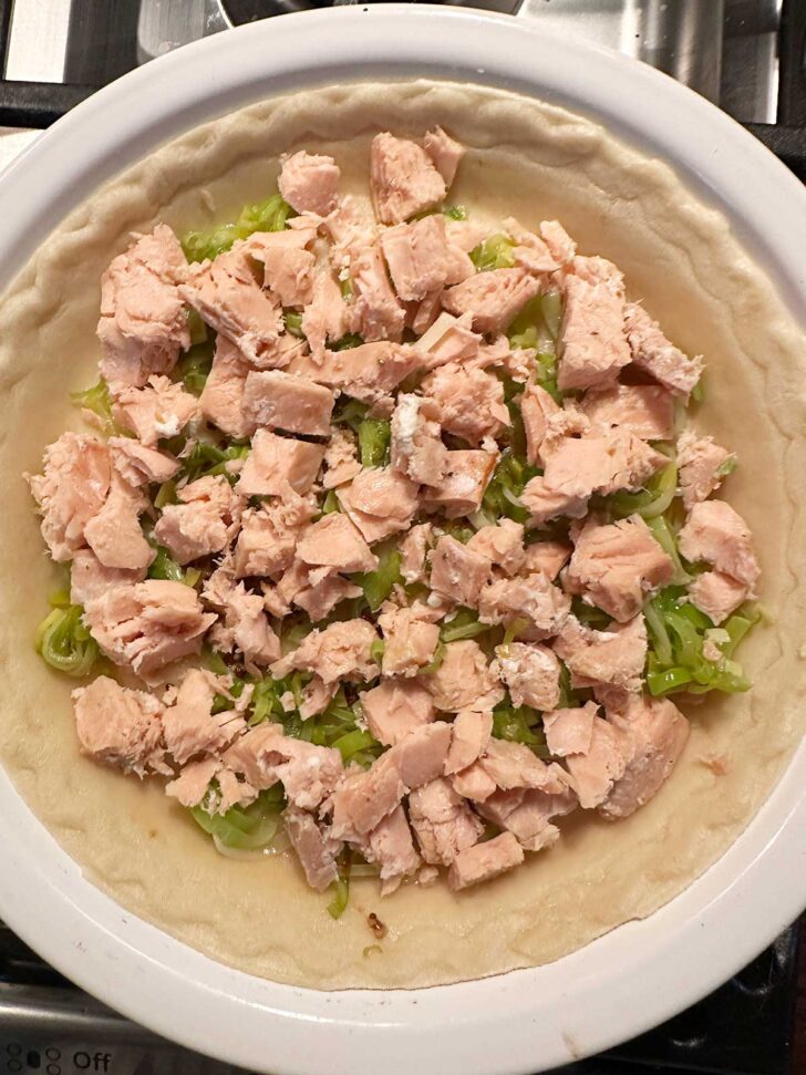 Adding cooked salmon to pie shell.