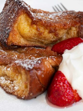 Caramelized French toast on plate with strawberries and whipped cream.
