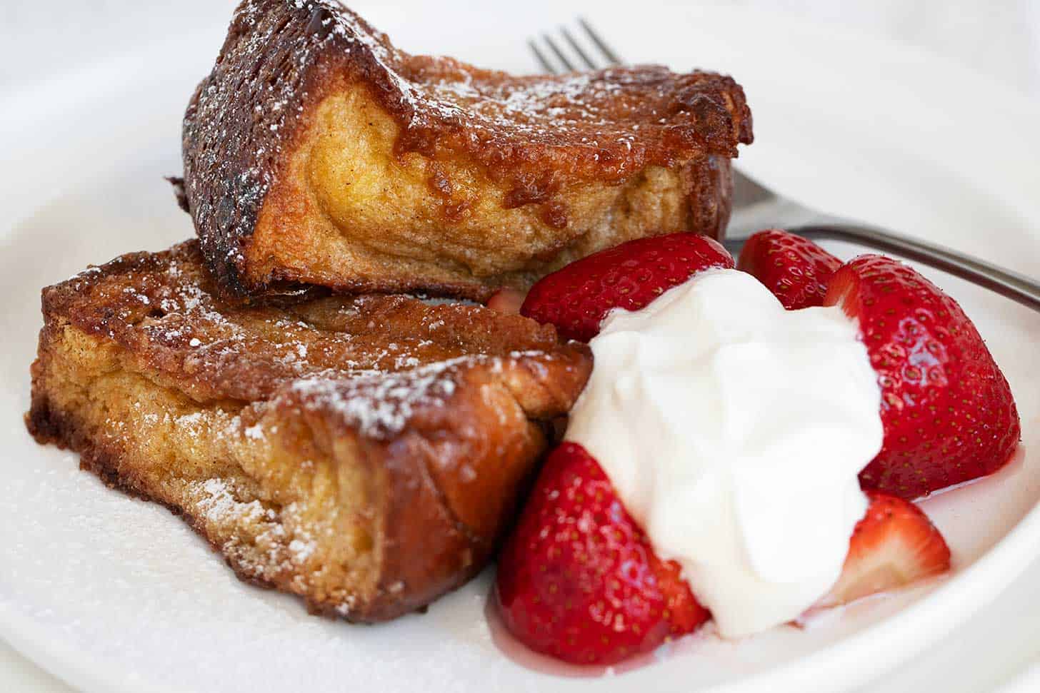 Caramelized French toast on plate with strawberries and whipped cream.