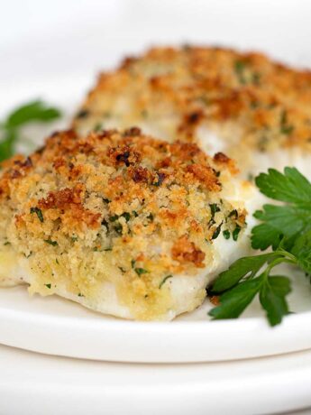 Panko crusted cod on plate with lemons and parsley.