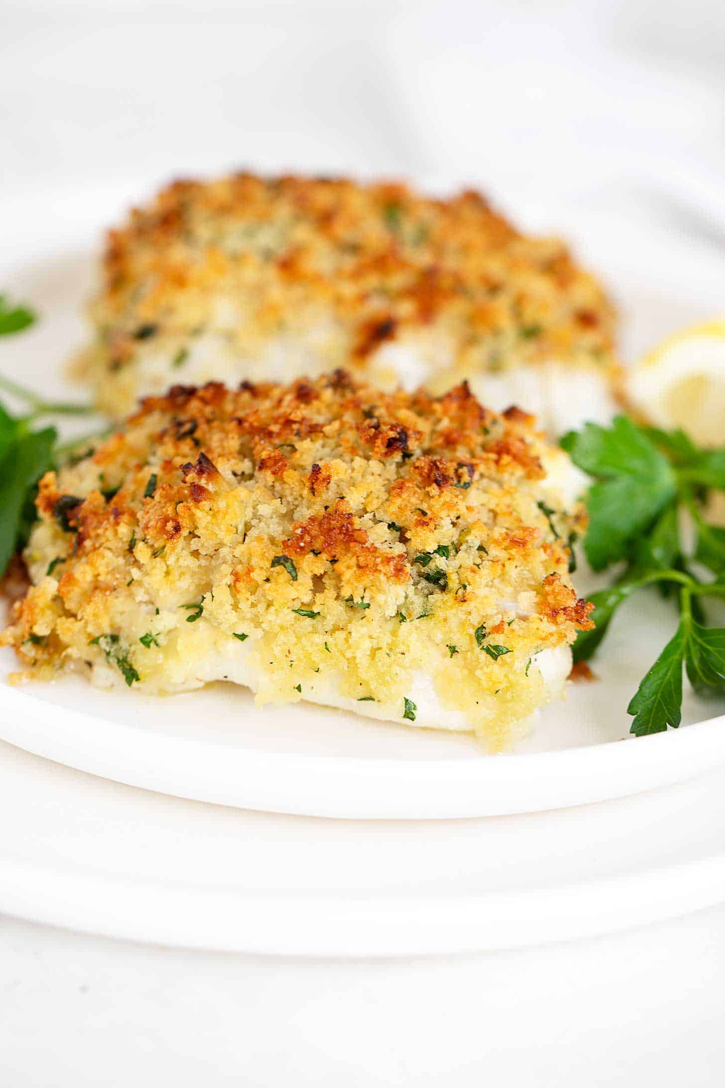 Panko-crusted cod on plate with parsley and lemon wedges.