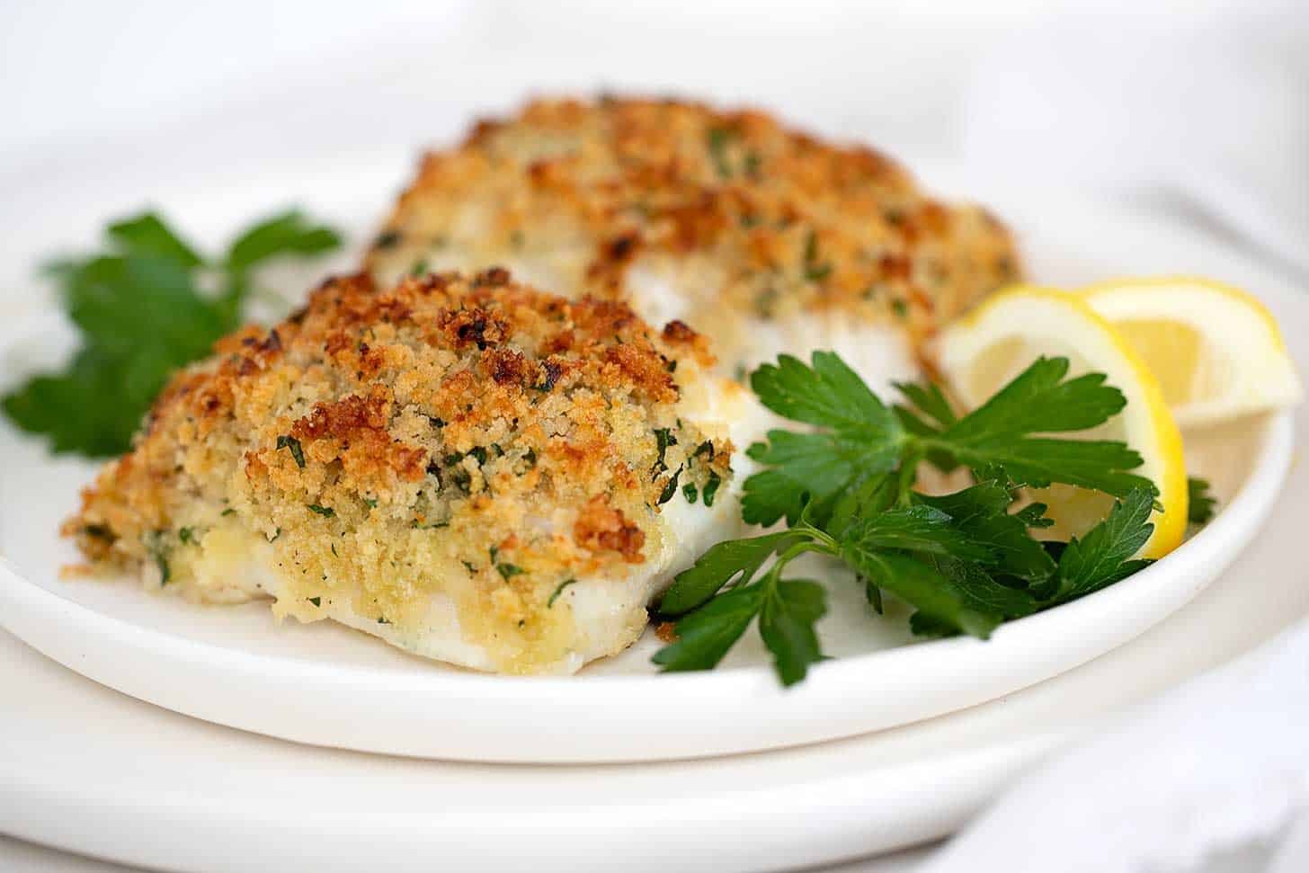 Panko crusted cod on plate with lemons and parsley.