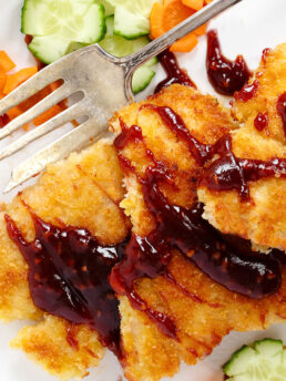 Salmon katsu with katsu sauce on a plate with vegetables.
