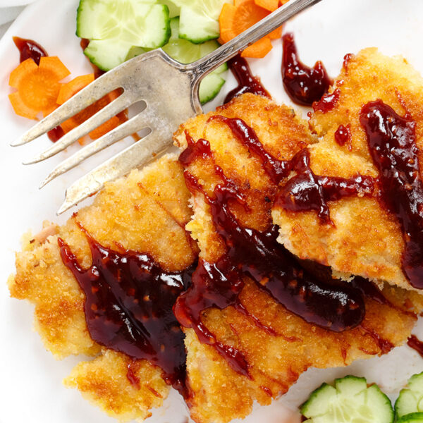 Salmon katsu with katsu sauce on a plate with vegetables.