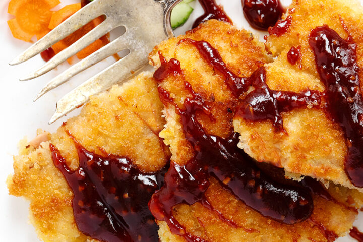 Salmon katsu with katsu sauce on a plate with vegetables.
