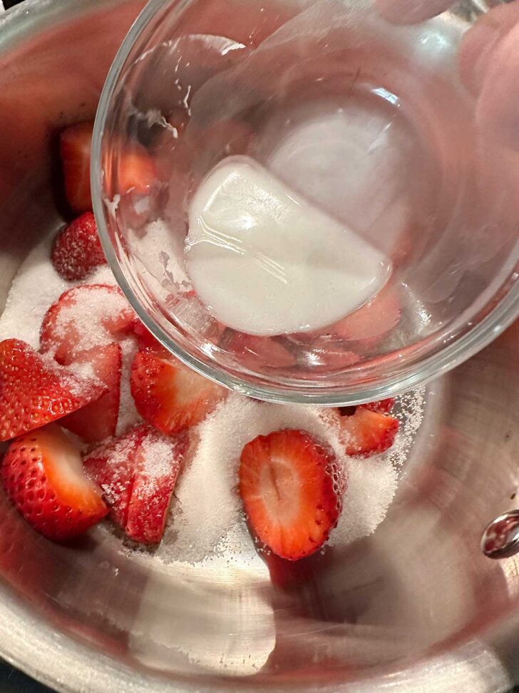 Adding cornstarch slurry to strawberries and sugar in saucepan.