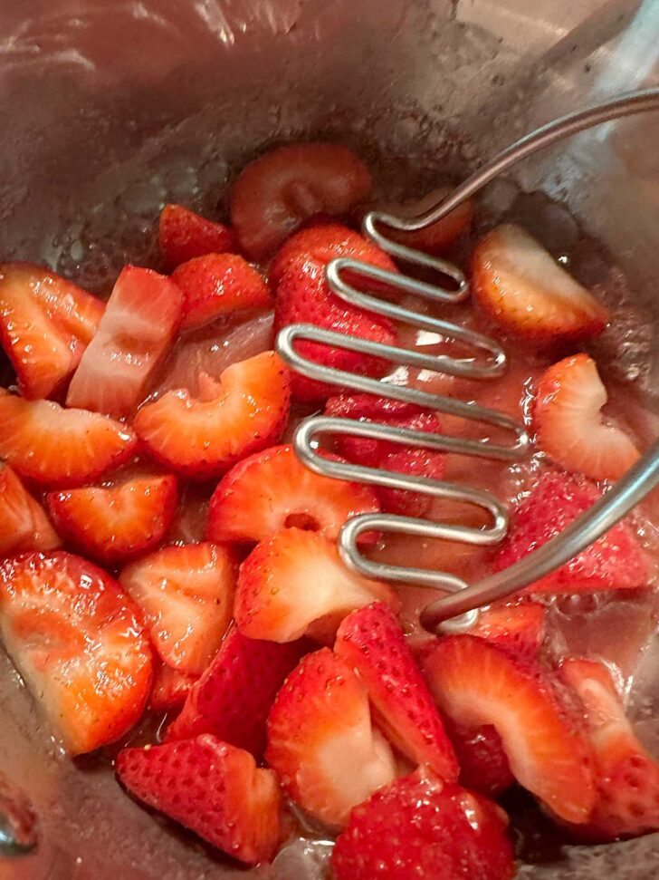Mashing the strawberries with a potato masher.