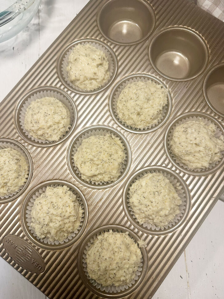 Lemon poppy seed muffin batter added to muffin cups in muffin tin.