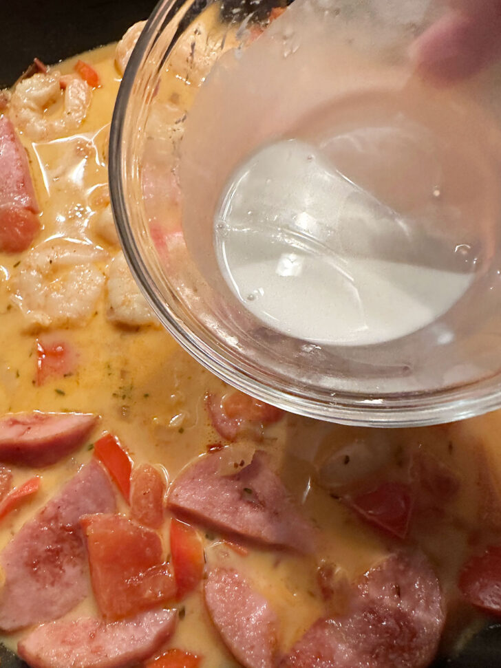 Adding cornstarch mixture to the sauce to thicken.