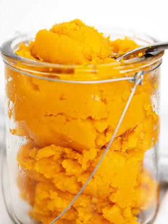 Homemade pumpkin puree in jar with spoon.