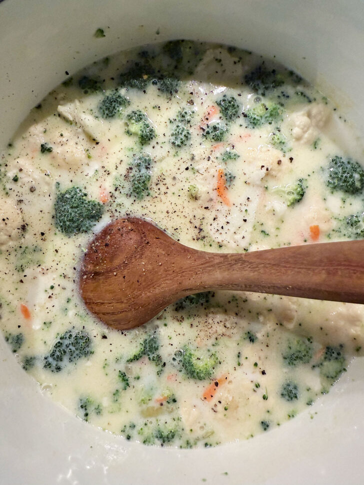 Seasoning the soup with salt and pepper, then simmering.
