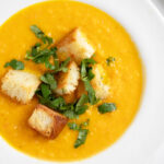 Carrot coriander soup in bowl with croutons.