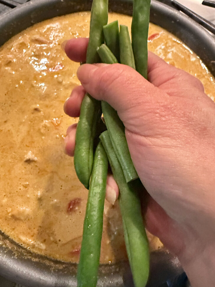 Adding green beans to the skillet.