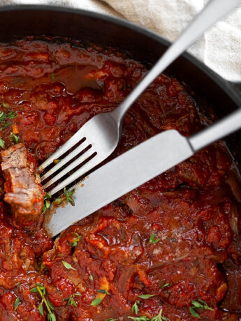 Swiss steak in skillet with fork and knife.