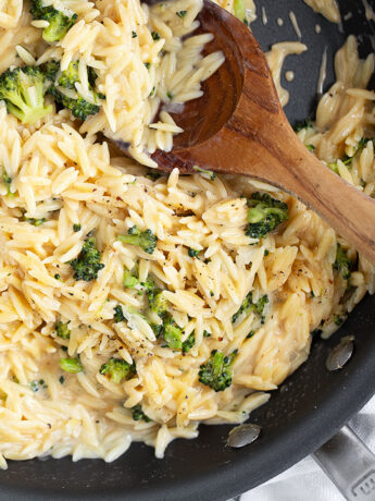 Broccoli cheddar orzo in skillet with a wooden spoon.