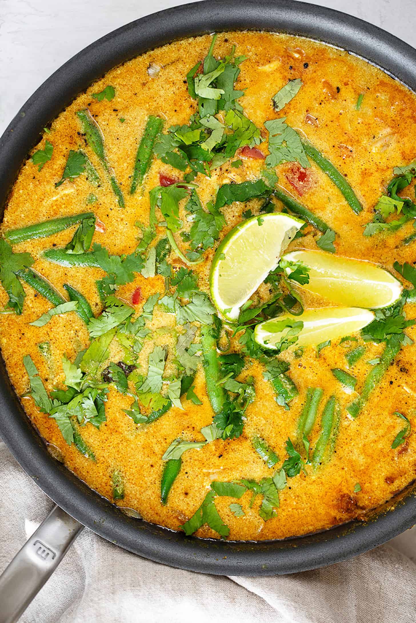 Chicken peanut butter curry in a skillet with lime slices.