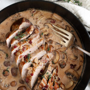 Pork tenderloin with a creamy mushroom and lingonberry jam sauce in skillet.