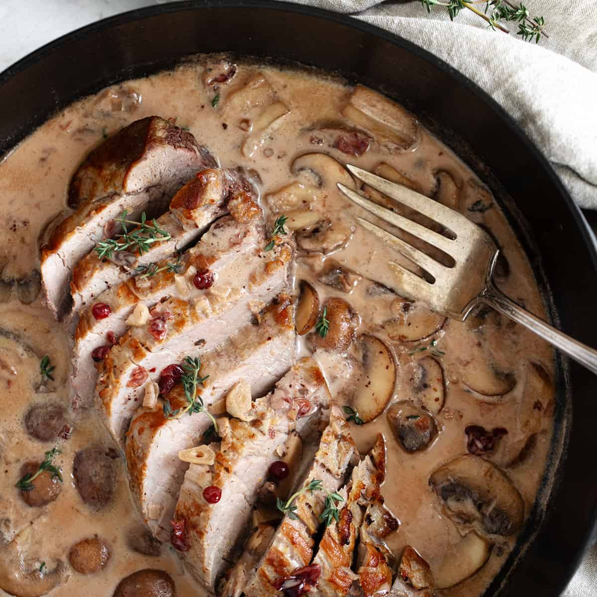 Pork tenderloin with a creamy mushroom and lingonberry jam sauce in skillet.