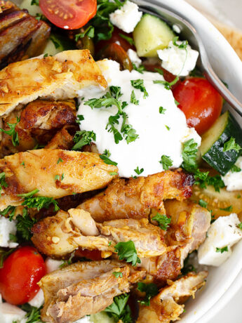 Chicken shawarma bowl with rice, tomatoes, cucumber and white sauce.