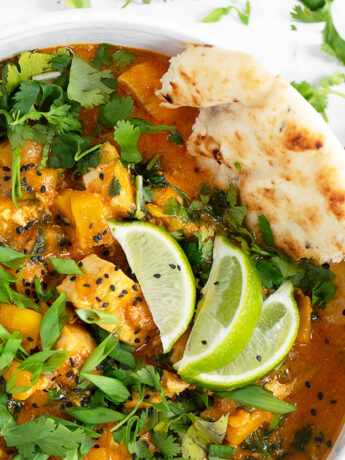 Chicken mango curry in serving bowl with naan bread.