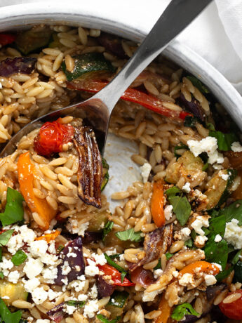 Roasted vegetable orzo in a serving bowl with a spoon.