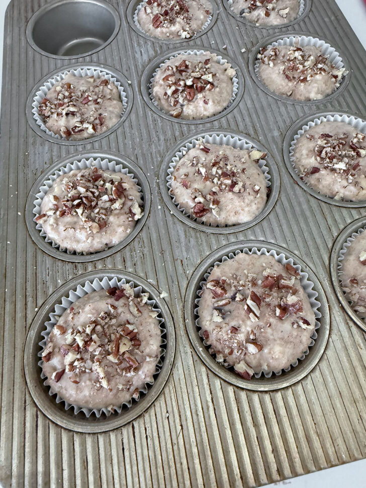 Muffin batter scooped into paper liners and topped with chopped nuts.
