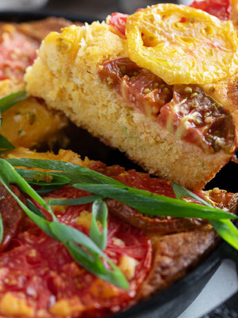Skillet cornbread topped with heirloom tomato in a cast iron skillet.