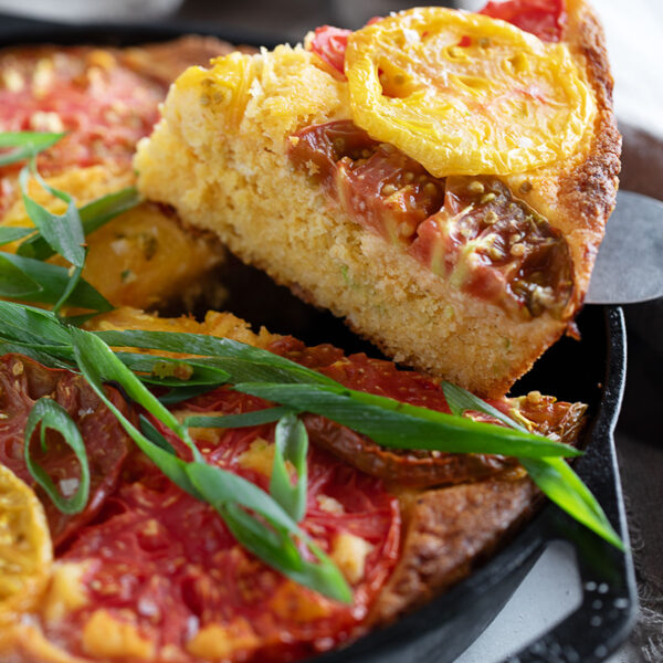 Skillet cornbread topped with heirloom tomato in a cast iron skillet.