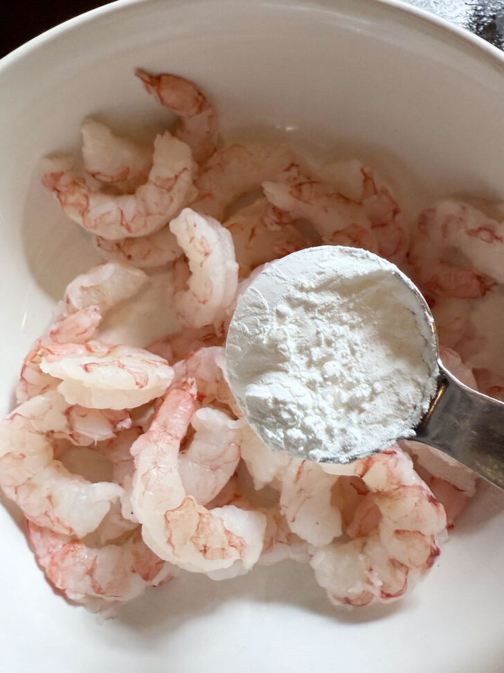 Adding cornstarch to the shrimp in a bowl.