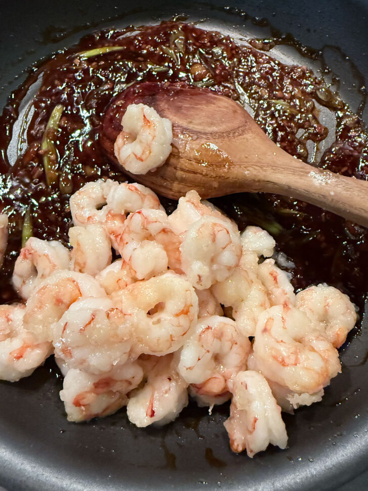 Adding the cooked shrimp to the skillet with the spicy orange sauce.