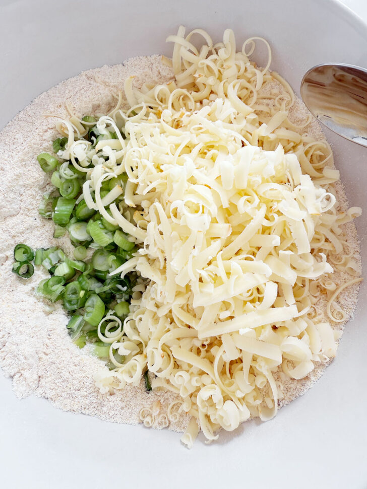 Green onion and shredded cheese added to the bowl with the dry ingredients.