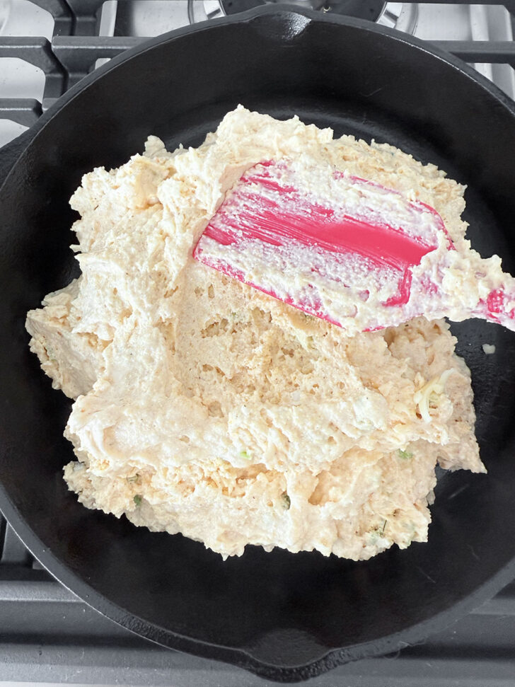 Spreading the mixed batter into a greased cast-iron skillet.