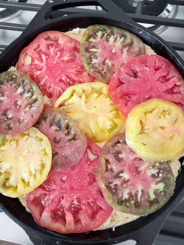 Topping the cornbread batter with sliced tomatoes before baking.