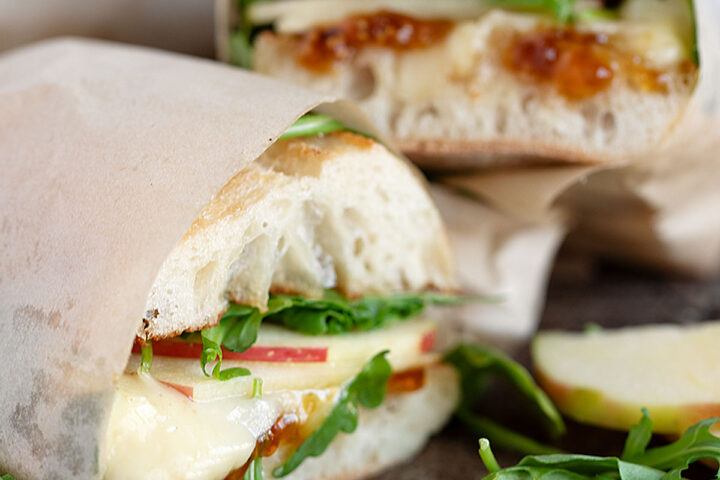 Apple, brie and fig jam sandwiches on a serving board.