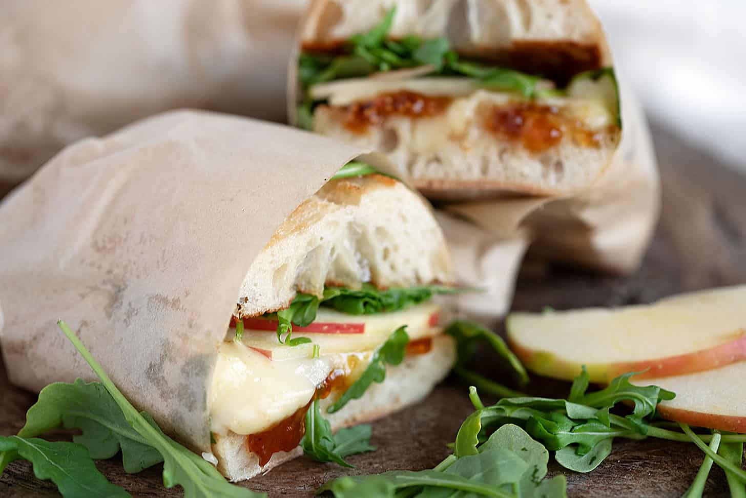 Apple, brie and fig jam sandwiches on a serving board.