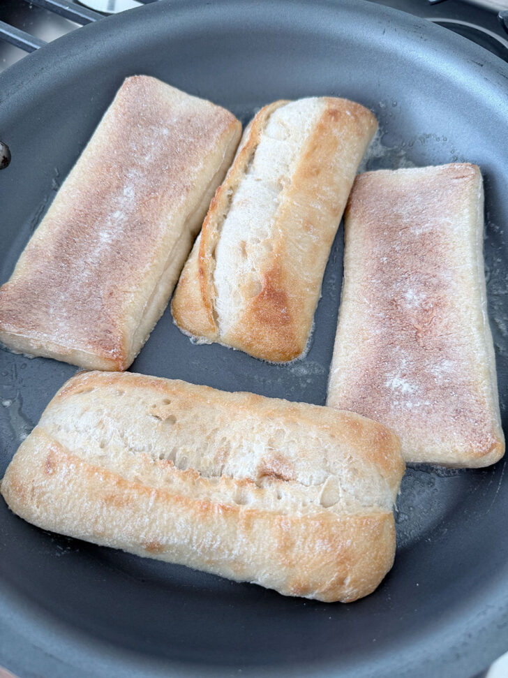 Ciabatta rolls placed in skillet cut side down.