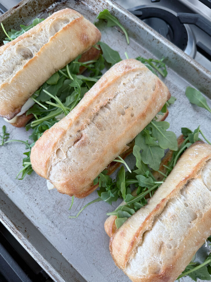 Top of the ciabatta buns placed on top of the sandwiches to finish the apple Brie sandwiches.