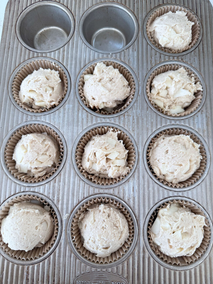 Apple muffin batter scooped into muffin cups.