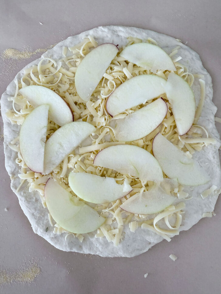 Pizza dough topped with shredded smoked cheddar and apple slices.