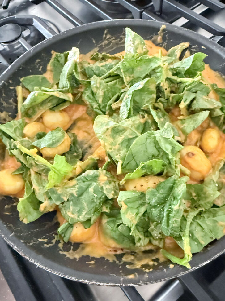 Adding the spinach to the gnocchi in the skillet.