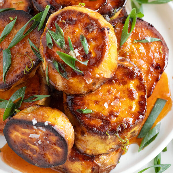 Melting sweet potatoes on a plate with a honey sriracha sauce.
