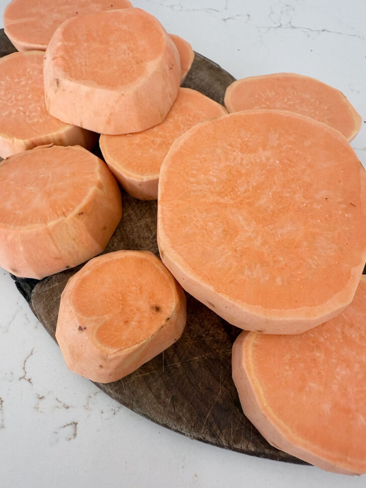 Peeled and sliced sweet potatoes on a cutting board.