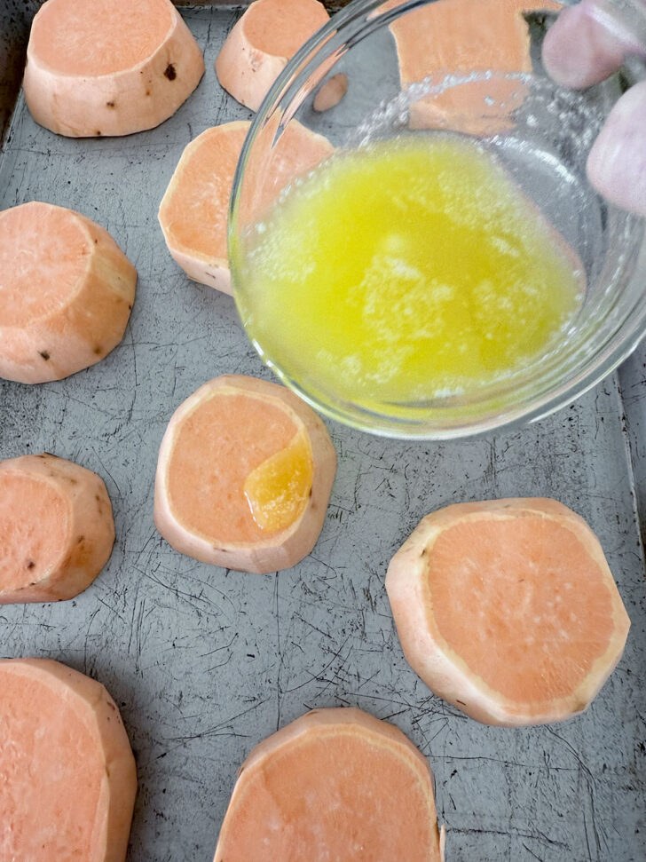 Drizzling melted butter over the sweet potato slices on a baking sheet.