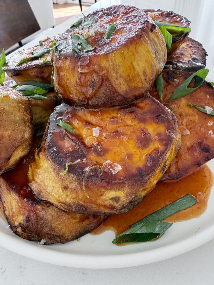 Honey sriracha melting sweet potatoes on a plate garnished with green onion and flaky salt.