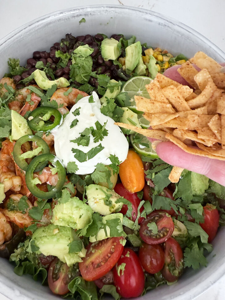 Sprinkling tortilla strips over the salad.