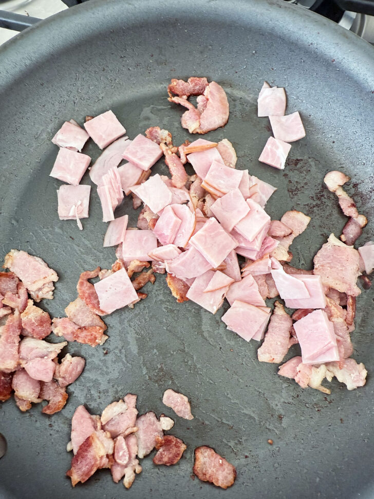 Ham added to cooked bacon in a skillet.