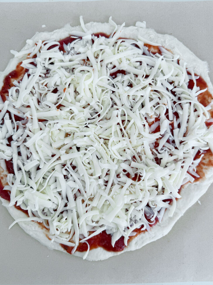 Pizza dough topped with pizza sauce and shredded mozzarella cheese.