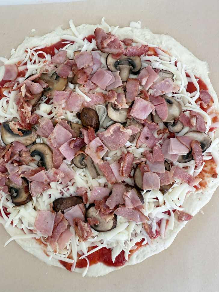 Precooked bacon and ham added to the top of the pizza.
