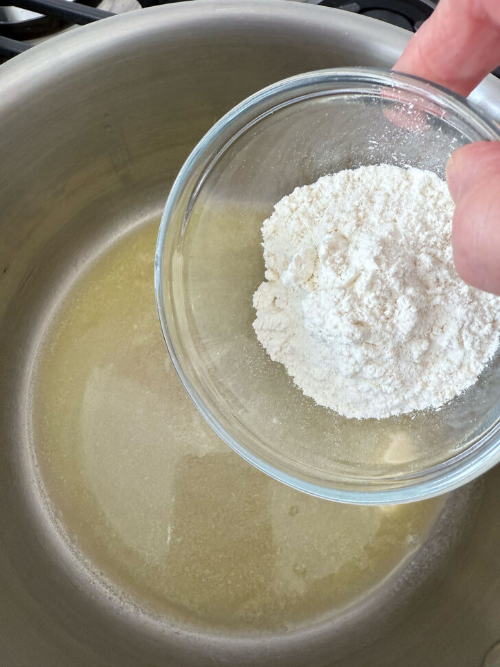 Adding flour to the melted butter in a saucepan.