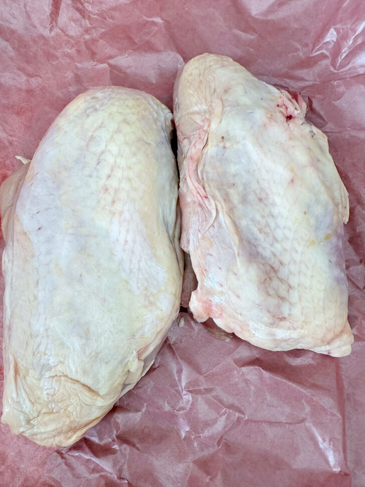 Boneless skin on chicken breasts on butcher paper.
